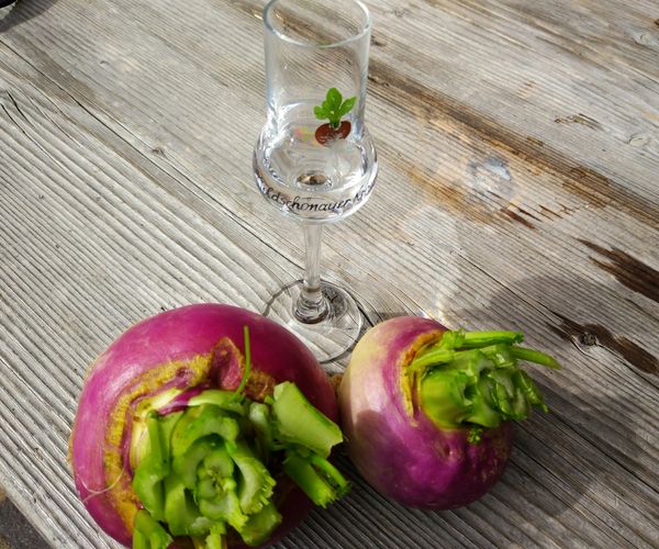 Zwei pinkfarbene Krautingerrüben liegen auf einem Holztisch neben einem Schnapsglas mit einem grünen Blatt.