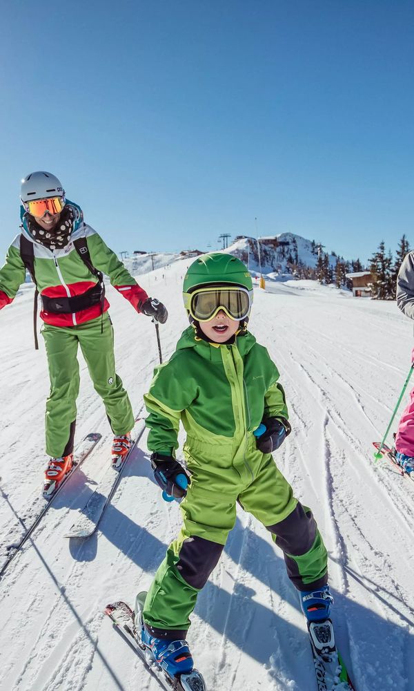 Eine Gruppe von vier Skifahrern, darunter Kinder und Erwachsene, steht auf einer präparierten Skipiste unter strahlendem Sonnenschein.